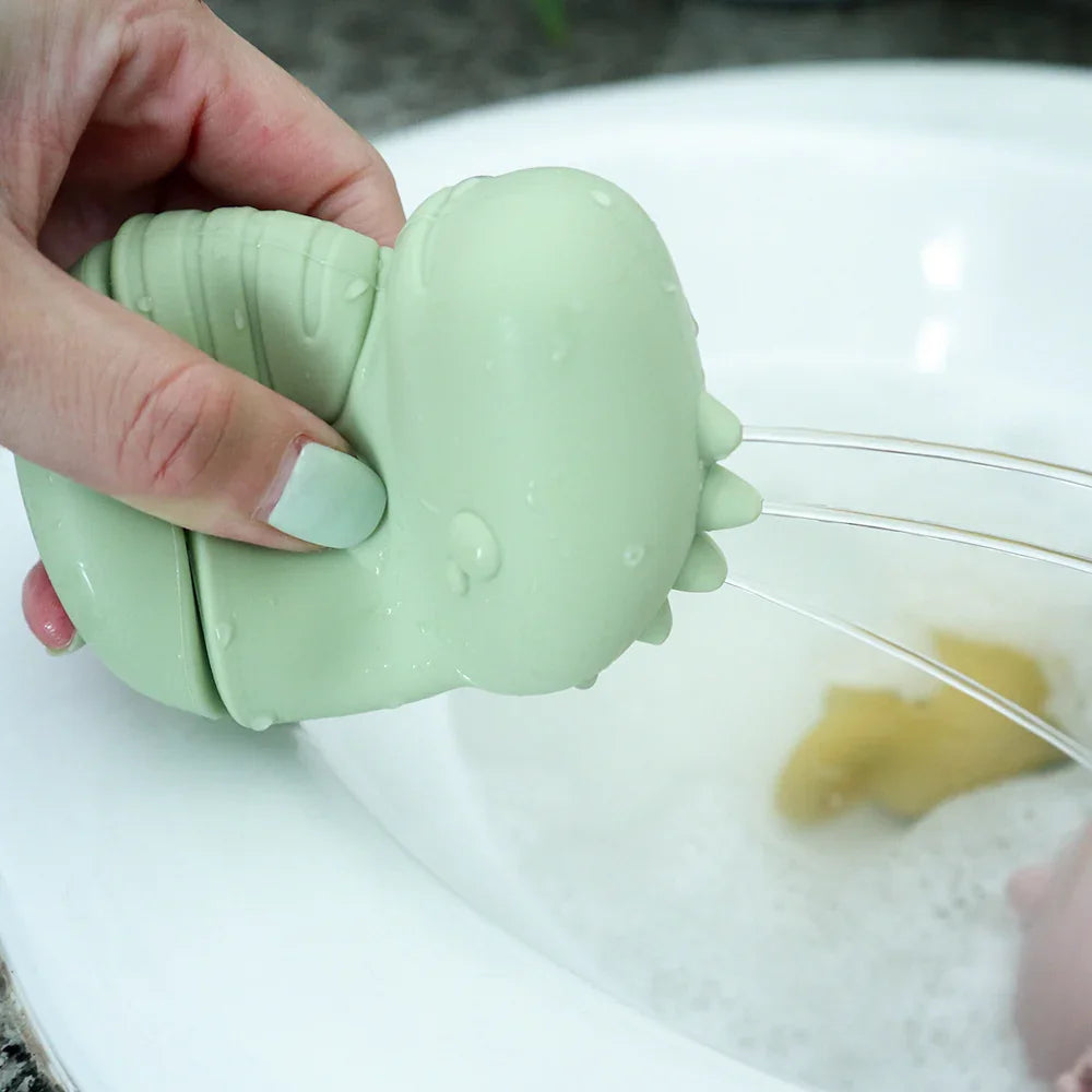 Juguete de baño de silicona verde vertiendo agua en el lavabo.